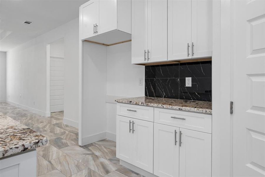 Kitchen with backsplash, light stone countertops, and white cabinets