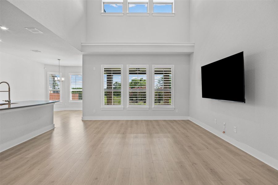 A spacious, naturally illuminated great room featuring high ceilings and elegant flooring, seamlessly connecting to the kitchen.