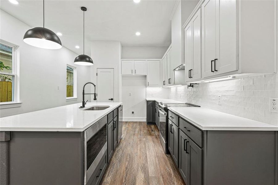 Kitchen featuring white cabinets, stainless steel appliances, dark wood-style floors, gray cabinetry, and an island with sink