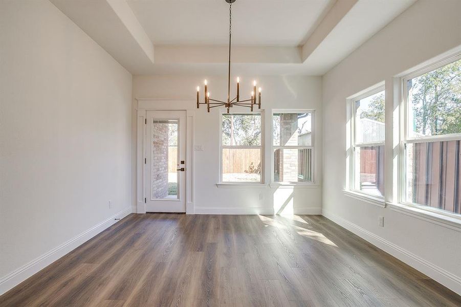 Unfurnished dining area featuring dark wood-style floors, a chandelier, and a raised ceiling