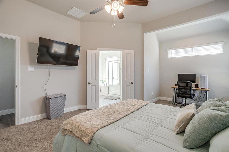 Carpeted primary bedroom with ceiling fan, seating area and natural light