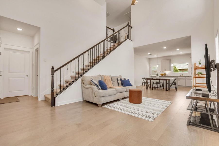 This spacious, open-concept living area features a cozy seating arrangement, modern staircase, and abundant natural light. The adjacent kitchen and dining area offer a seamless flow for entertaining. Neutral tones and hardwood floors create a warm, inviting atmosphere.