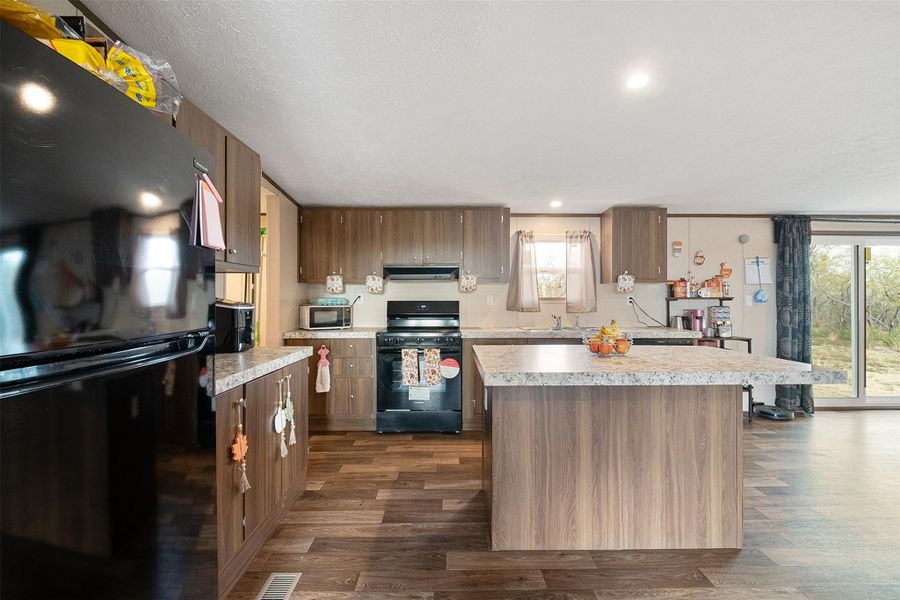 Kitchen featuring black appliances, light countertops, a kitchen island, dark wood-style floors, and recessed lighting