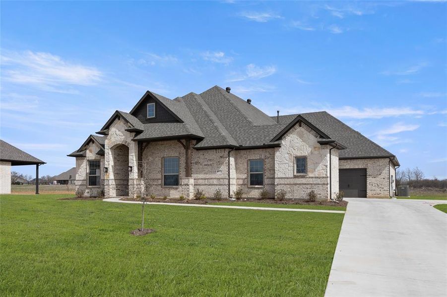 French country inspired facade featuring brick siding, roof with shingles, concrete driveway, a front lawn, and central AC French country inspired facade featuring brick siding, roof with shingles, concrete driveway, a front lawn, and central AC