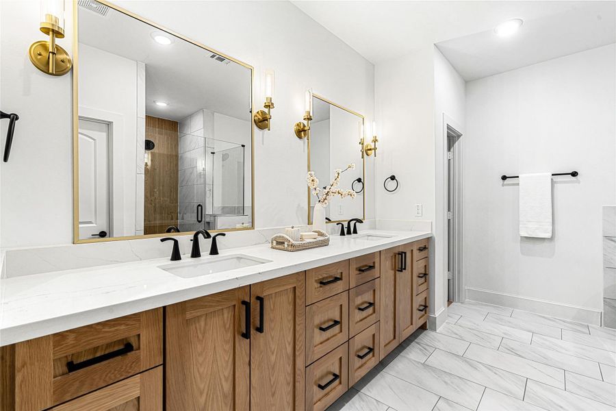 Luxurious primary bathroom featuring a double vanity with quartz countertops, modern matte black fixtures, and elegant gold-accented mirrors - combining warmth and sophistication in one space.