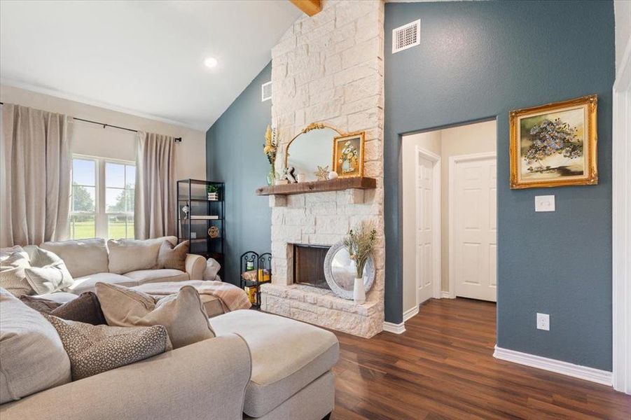 Living area with high vaulted ceiling, dark wood-type flooring, a stone fireplace, and beamed ceiling