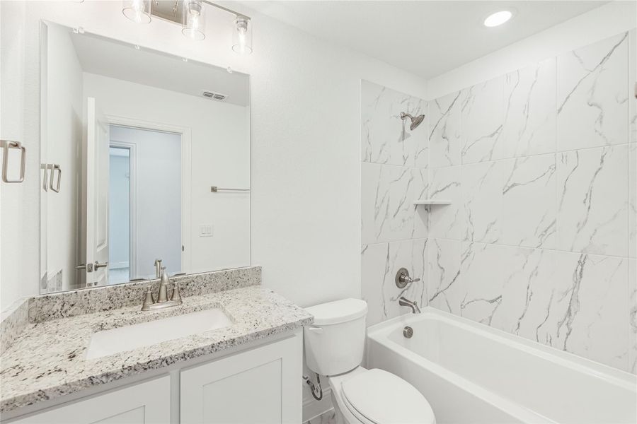 Bathroom with granite countertop vanity, white tub, and marble-style tile shower surround Bathroom with granite countertop vanity, white tub, and marble-style tile shower surround