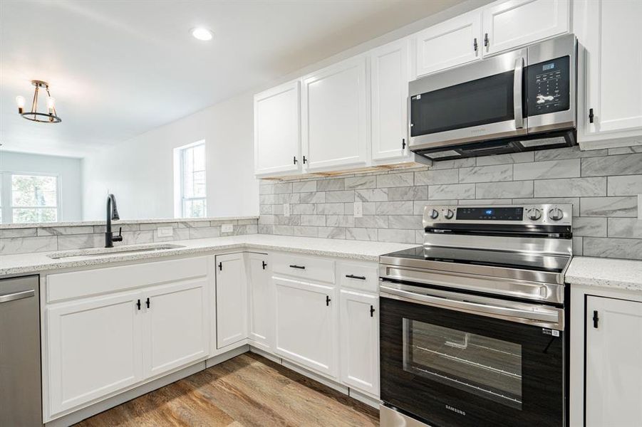 Kitchen with tasteful backsplash, sink, light stone countertops, appliances with stainless steel finishes, and light hardwood / wood-style flooring