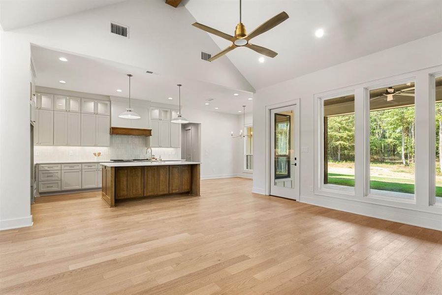Kitchen featuring glass insert cabinets, an island with sink, backsplash, high vaulted ceiling, and open floor plan