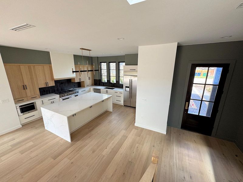 Kitchen with light wood finished floors, visible vents, tasteful backsplash, a center island, and appliances with stainless steel finishes