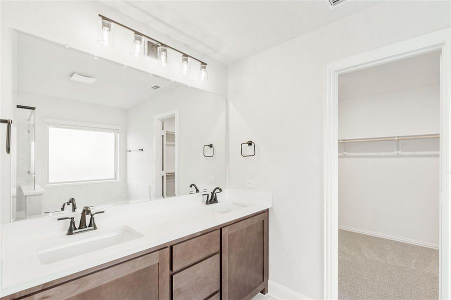 Bathroom with double sink vanity, dark wood cabinets, white countertop, and walk-in closet entrance nearby.