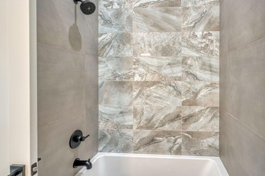 Textured tile walls and matte black hardware elevate this sleek modern shower and tub combination. Textured tile walls and matte black hardware elevate this sleek modern shower and tub combination.