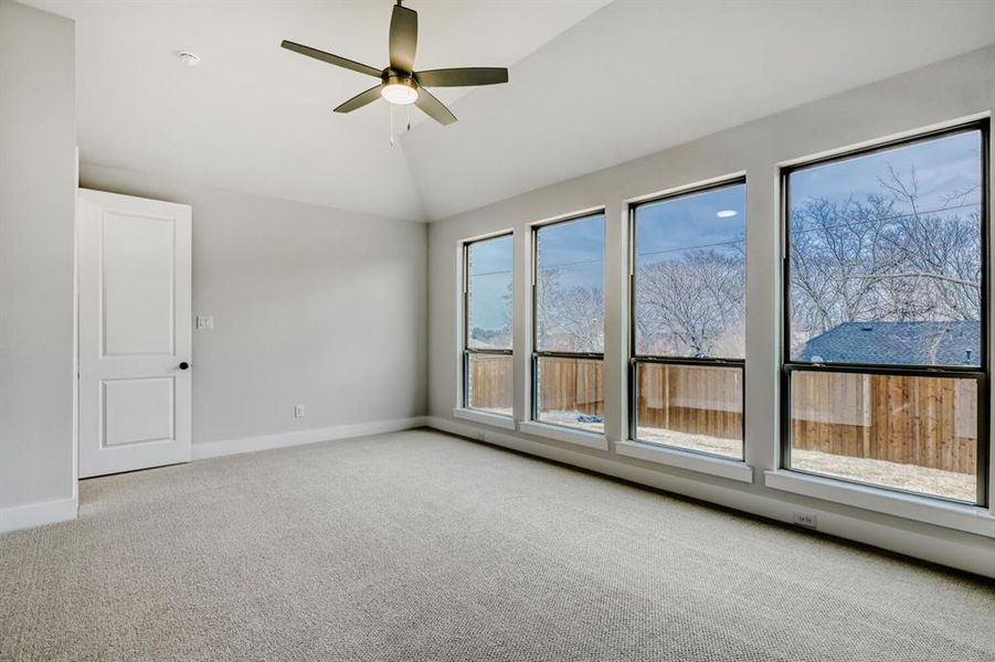 Empty room featuring light carpet, a ceiling fan, and vaulted ceiling
