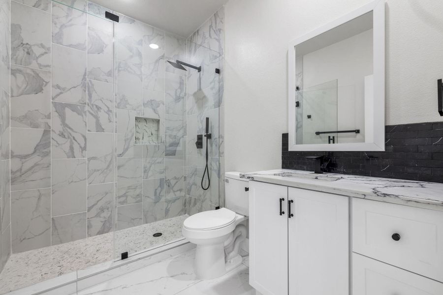 Bathroom with decorative backsplash, tiled walk in shower and vanity.