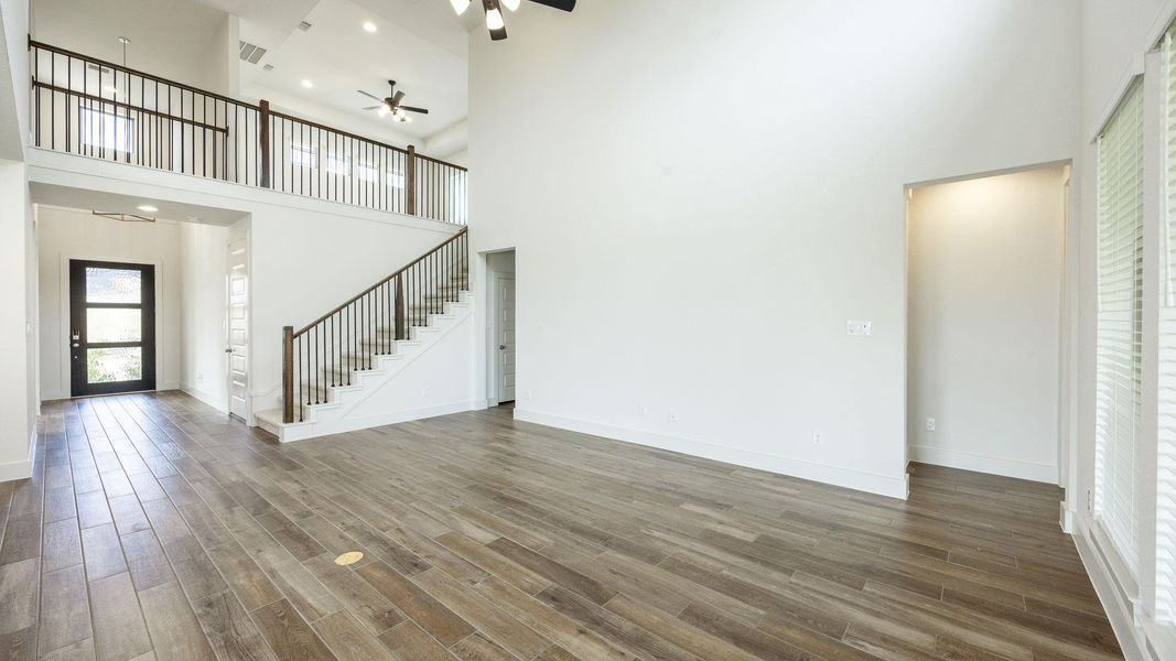 Unfurnished living room featuring a high ceiling, wood finished floors, ceiling fan, stairs, and recessed lighting