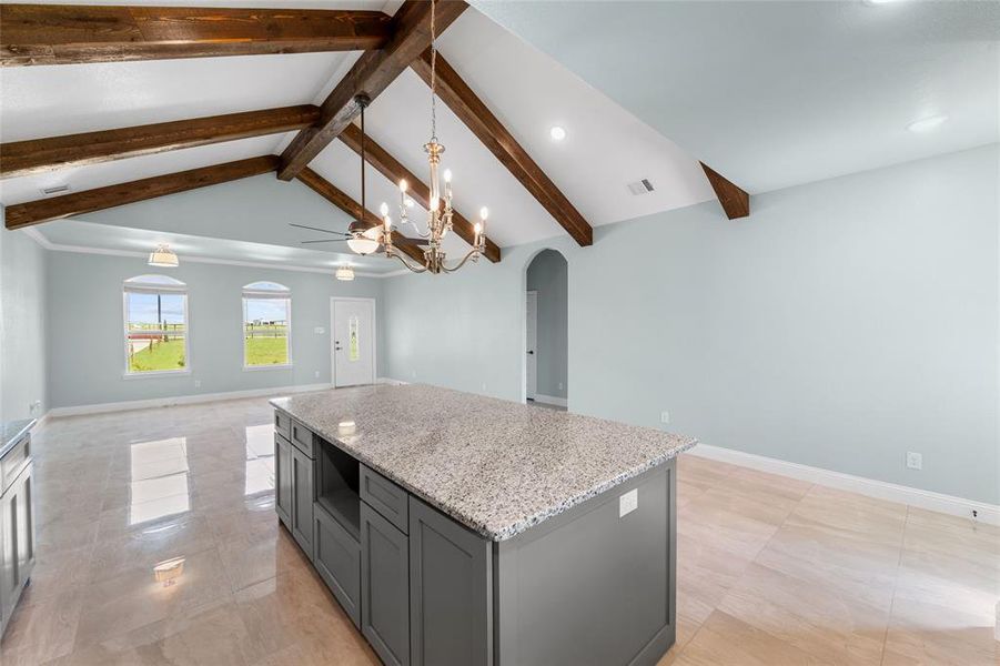 Kitchen with vaulted ceiling with beams, light tile patterned floors, a kitchen island, gray cabinets, and light stone countertops