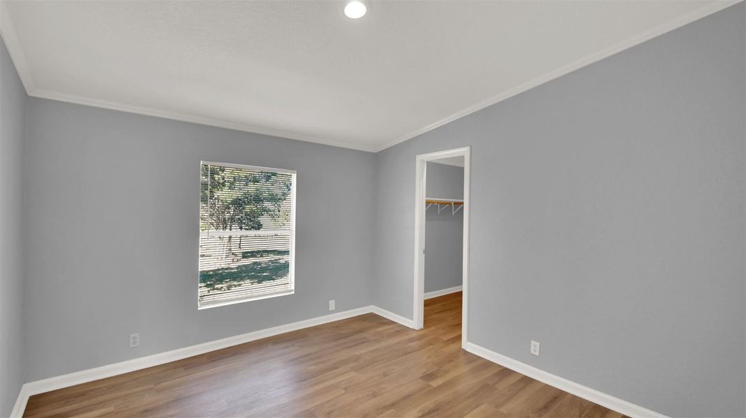 Unfurnished bedroom featuring a walk in closet, crown molding, and light wood-style floors