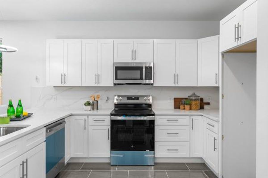 Kitchen featuring stainless steel appliances, white cabinets, light stone counters, and dark tile patterned floors Kitchen featuring stainless steel appliances, white cabinets, light stone counters, and dark tile patterned floors