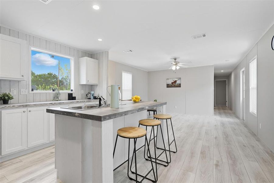 Kitchen featuring white cabinetry, recessed lighting, a kitchen breakfast bar, light wood-style flooring, and an island with sink Kitchen featuring white cabinetry, recessed lighting, a kitchen breakfast bar, light wood-style flooring, and an island with sink