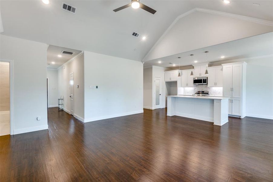 Unfurnished living room with high vaulted ceiling, ceiling fan, crown molding, and dark wood-type flooring