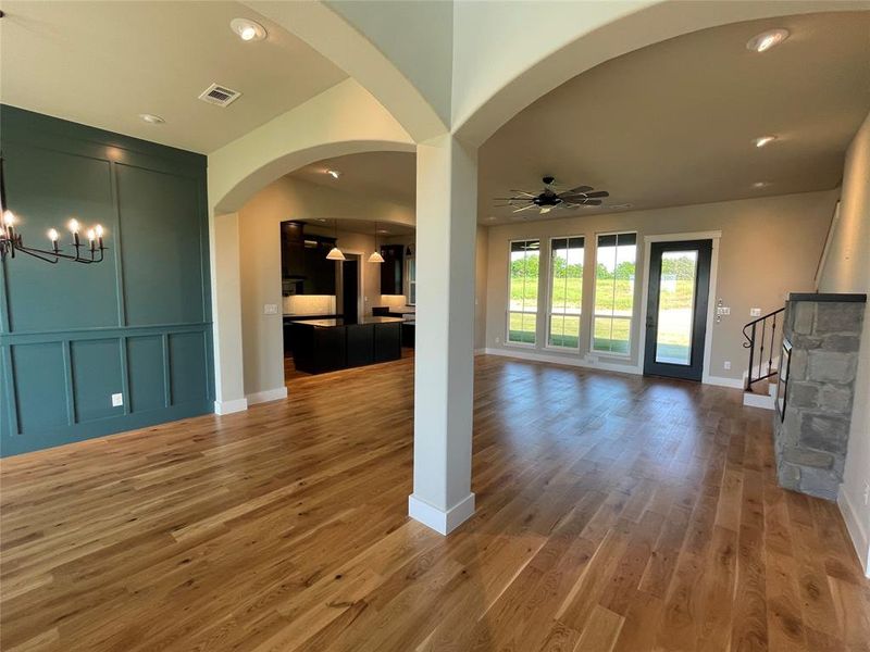 Expansive open-concept interior featuring light wood-finish flooring, arched doorways, a board and batten accent wall, recessed lighting, and large windows