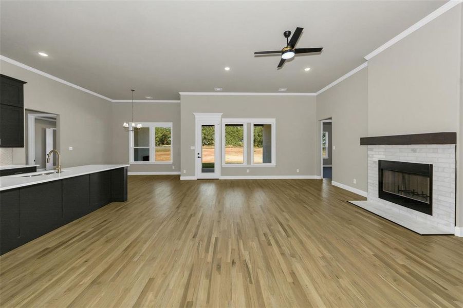 Unfurnished living room featuring crown molding, recessed lighting, a chandelier, light wood-style flooring, and a brick fireplace