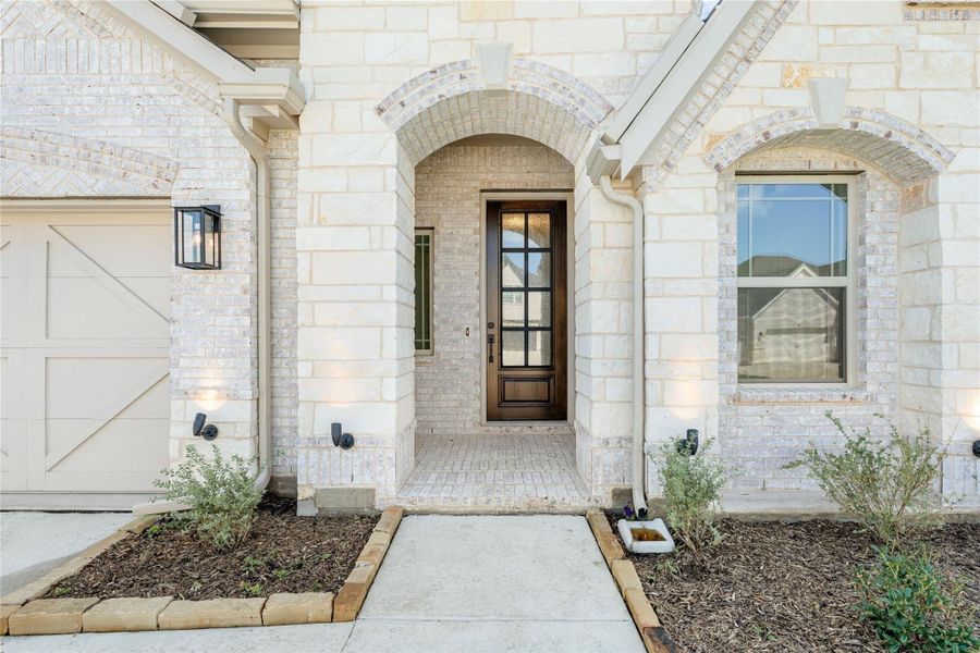 Home entrance with arched stone surround, wood and glass front door, and brick exterior