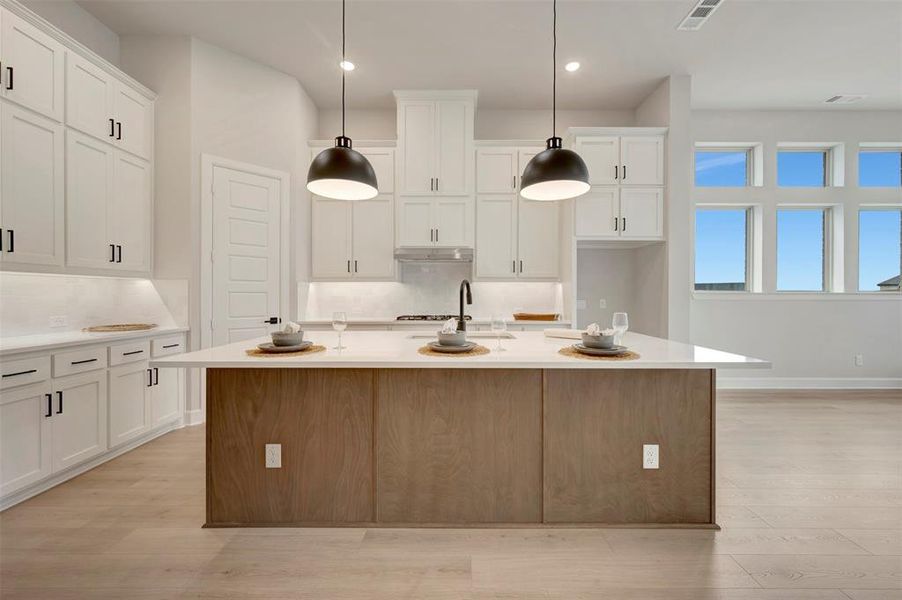 Dual tone kitchen featuring a kitchen island with sink, pendant lighting, light stone counters, light wood-style floors, and two tone color scheme