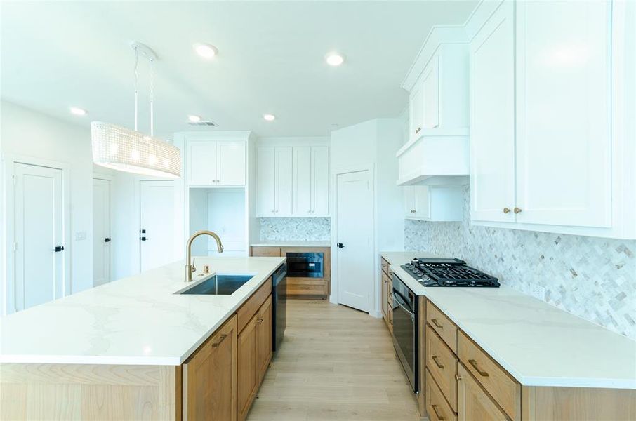 Kitchen with a kitchen island with sink, white cabinets, light wood-style flooring, light stone counters, and stainless steel oven