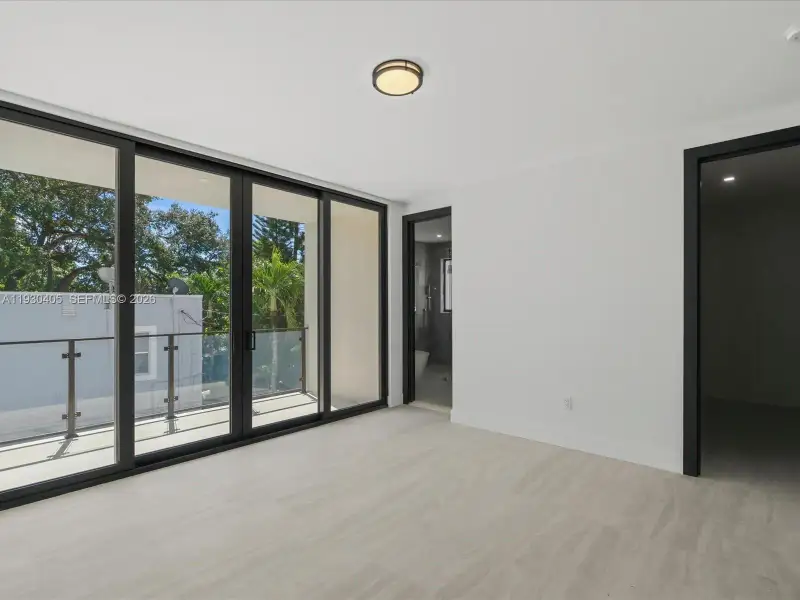 Floor-to-ceiling sliding glass doors, neutral stone-finish flooring, private balcony with glass railing, and dark-finish door frames Floor-to-ceiling sliding glass doors, neutral stone-finish flooring, private balcony with glass railing, and dark-finish door frames
