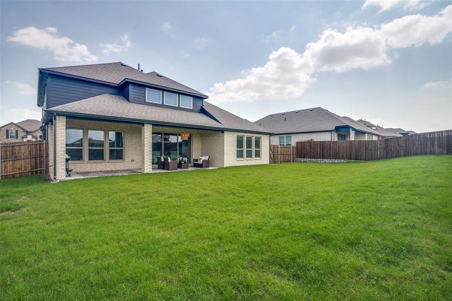 Expansive backyard with a manicured lawn, full privacy fencing, and a covered patio featuring brick columns and a sliding glass door