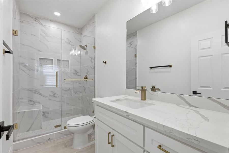 Upstairs bathroom featuring double vanity, large mirror, and frameless glass walk in shower with marble look tile.