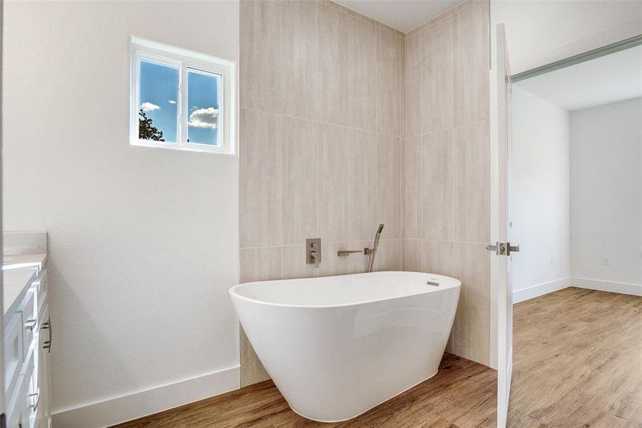 Full bathroom with vanity, a freestanding bath, light wood finished floors, and tile walls Full bathroom with vanity, a freestanding bath, light wood finished floors, and tile walls