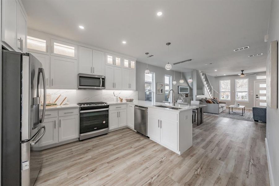 Kitchen featuring decorative light fixtures, white cabinetry, sink, kitchen peninsula, and stainless steel appliances