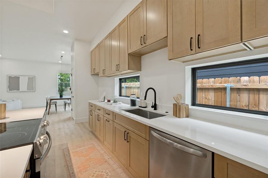 Modern kitchen featuring abundant light wood-finish cabinetry, sleek stainless steel appliances, a single-basin sink with a matte black faucet, and light-toned countertops
