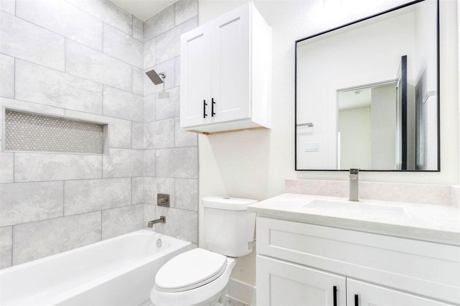 This secondary bathroom offers a shower-tub combo with large-format tile surrounds and a crisp white vanity.