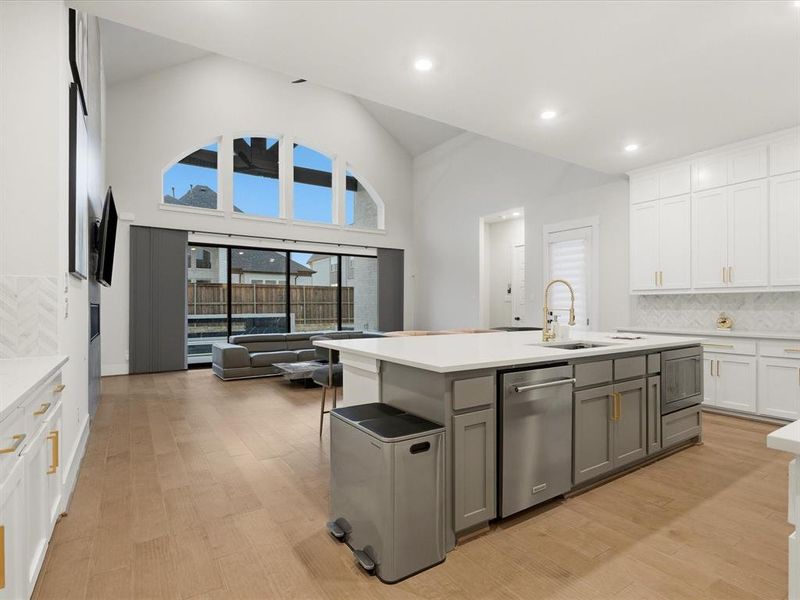 Open-concept living space featuring a spacious kitchen island with integrated sink, stainless steel dishwasher, and gold-tone faucet Open-concept living space featuring a spacious kitchen island with integrated sink, stainless steel dishwasher, and gold-tone faucet