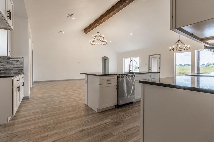 Kitchen featuring light hardwood / wood-style flooring, an island with sink, hanging light fixtures, white cabinetry, and vaulted ceiling with beams