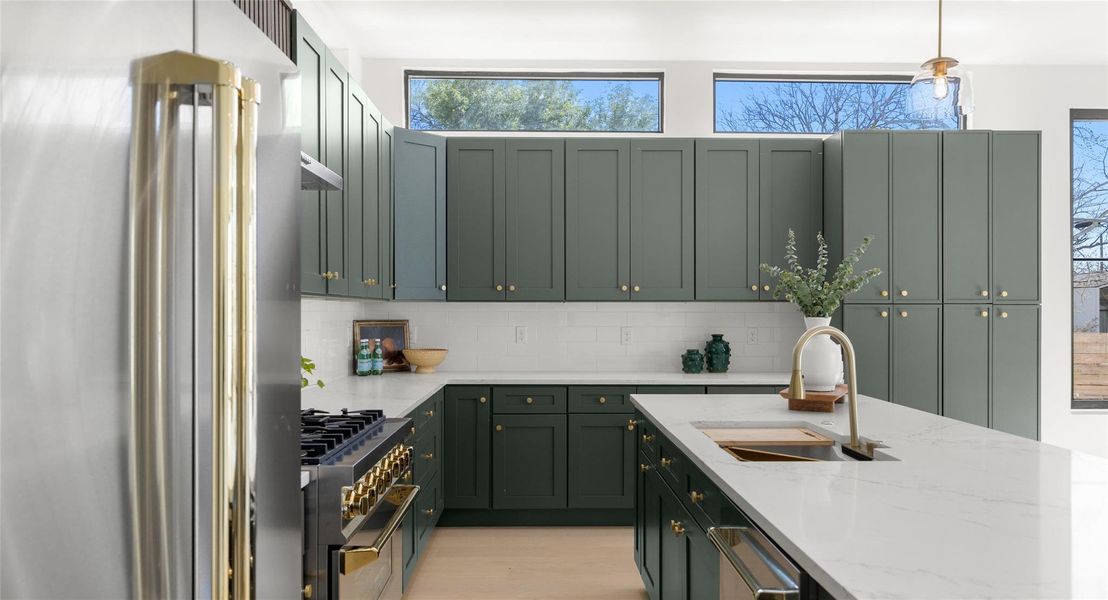 Kitchen featuring green cabinets, premium appliances, light stone counters, tasteful backsplash, and decorative light fixtures