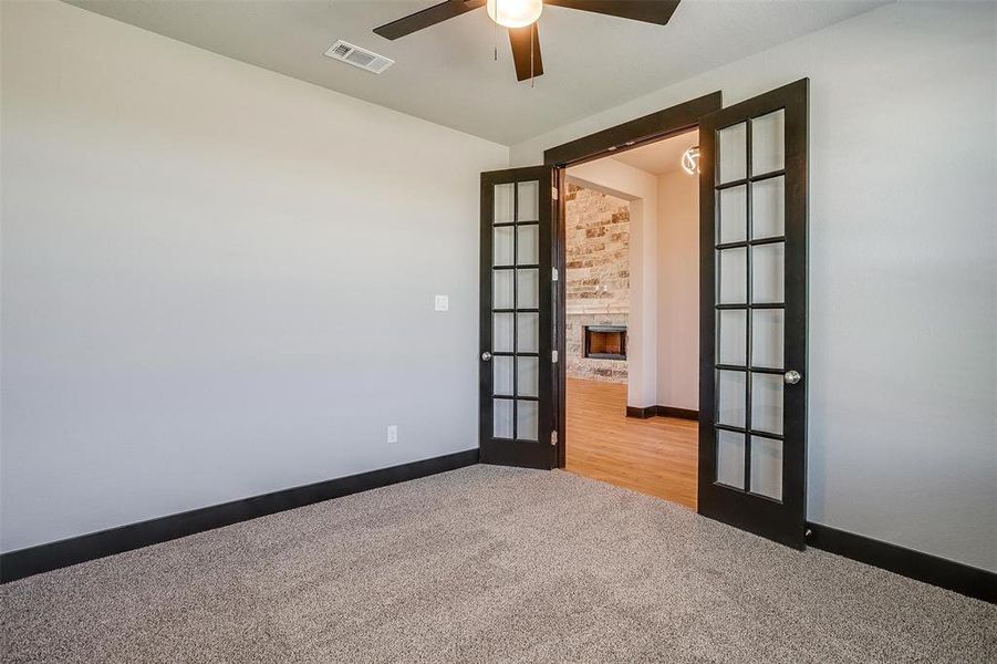 Spare room featuring a fireplace, light carpet, french doors, and ceiling fan