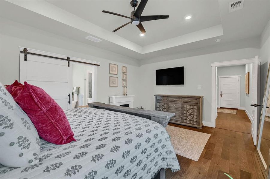 Bedroom featuring ceiling fan, dark hardwood / wood-style floors, a raised ceiling, and a barn door