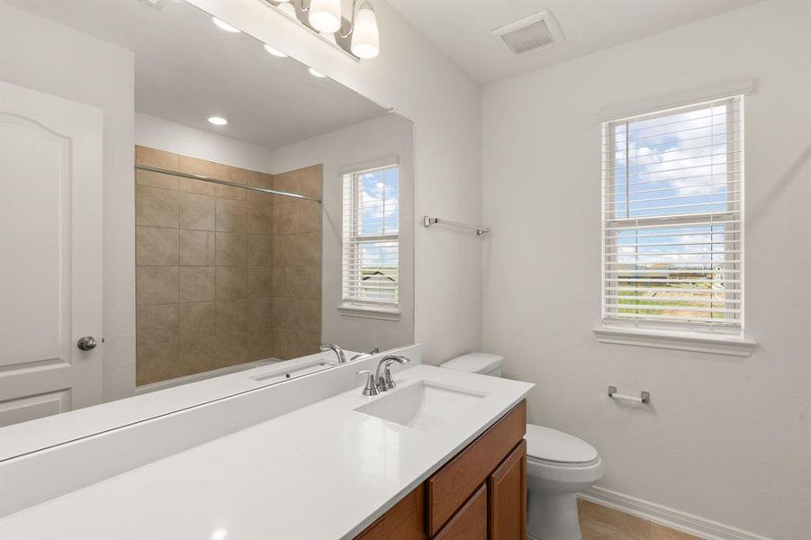 Secondary bathroom features light countertops and dark cabinets, neutral paint, shower/tub combo with tile surround, large mirror, tile floors, sleek fixtures and modern finishes, plenty of space to accommodate any visiting family or guests.