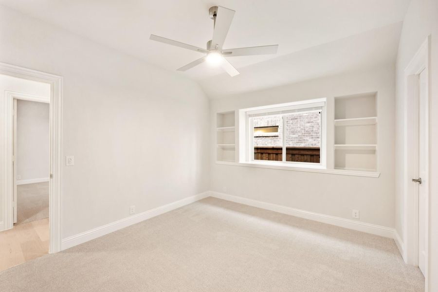 Empty bedroom with carpet, ceiling fan, and built-in shelves flanking a window