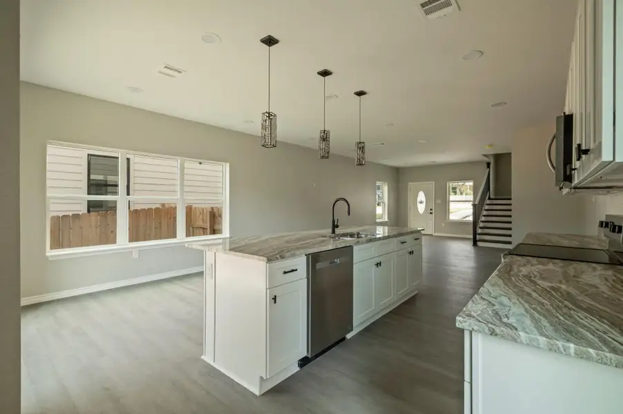 Kitchen featuring white cabinets, light stone countertops, stainless steel appliances, a center island with sink, and hanging light fixtures