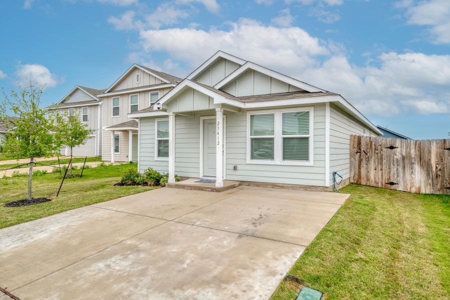 Light-colored siding exterior with a covered front porch, a concrete driveway, a wood fence, and a manicured lawn