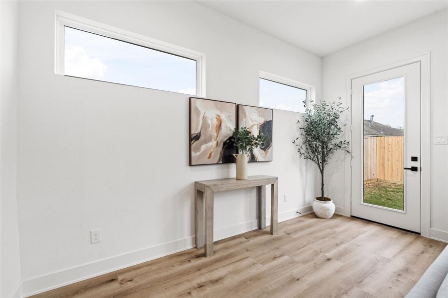 Slim transom windows and a full-view door flood the rear entry with soft natural light, creating a moment of calm between indoor comfort and outdoor living. Clean lines and oak-colored floors showcase Nima Homes’ mastery of balance—where every transition feels intentional and artfully composed.