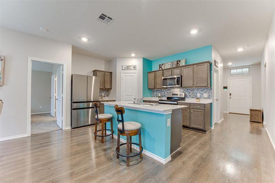 Kitchen with backsplash, a kitchen bar, a center island with sink, appliances with stainless steel finishes, and light wood-type flooring