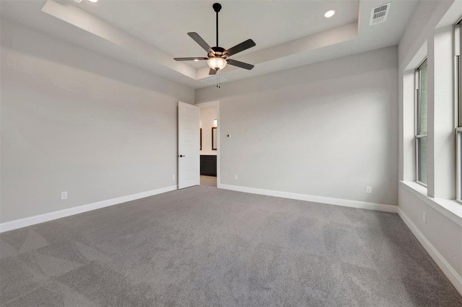 Spacious room featuring tray ceiling, recessed lighting, ceiling fan, plush gray carpeting, and multiple windows