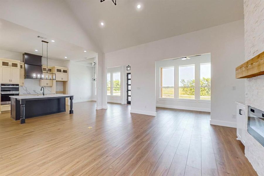 Living room with high vaulted ceiling, sink, a stone fireplace, and light hardwood / wood-style floors