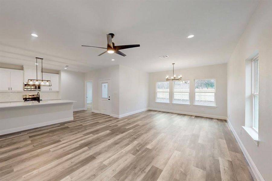 Unfurnished living room with sink, ceiling fan with notable chandelier, and light wood-type flooring